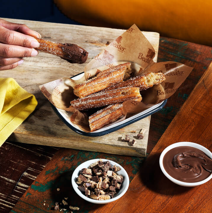  Beefeater dessert of churros with cinnamon sugar in a serving dish with pots of KitKat spread and crumbled KitKat pieces.
